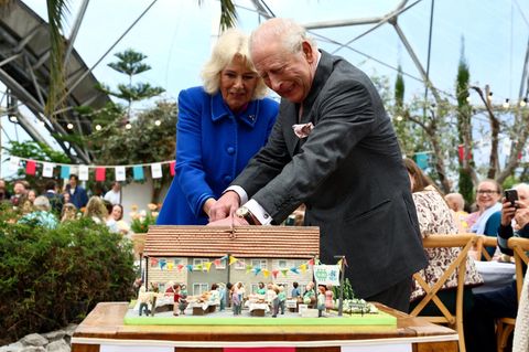 König Chalres und Camilla schneiden gemeinsam eine Torte in Form eines Hauses an