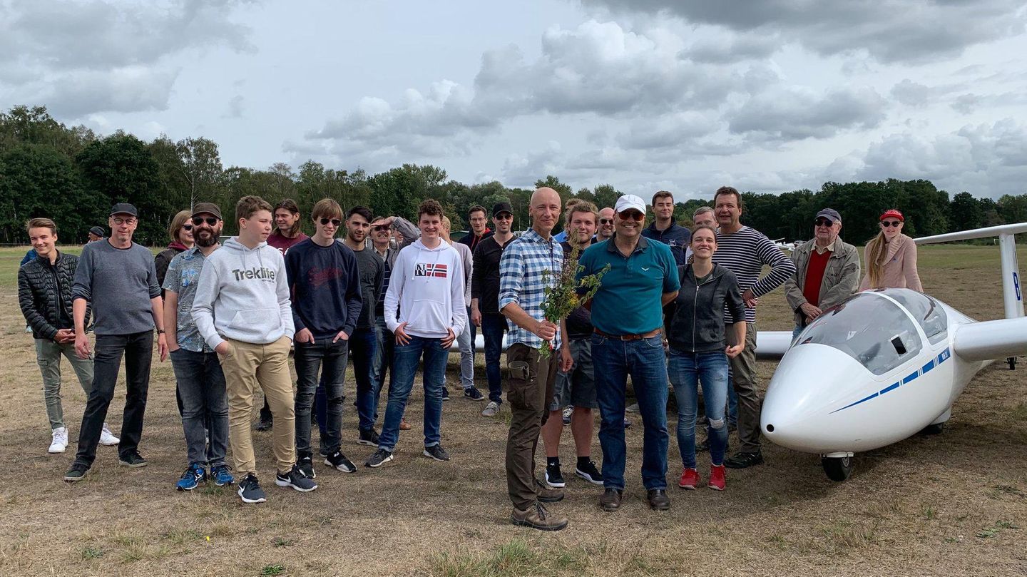 Eine Gruppe Menschen neben einem Segelflugzeug, einer hält einen Strauß Blumen in der Hand