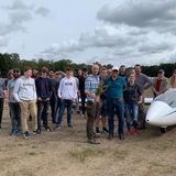 Eine Gruppe Menschen neben einem Segelflugzeug, einer hält einen Strauß Blumen in der Hand