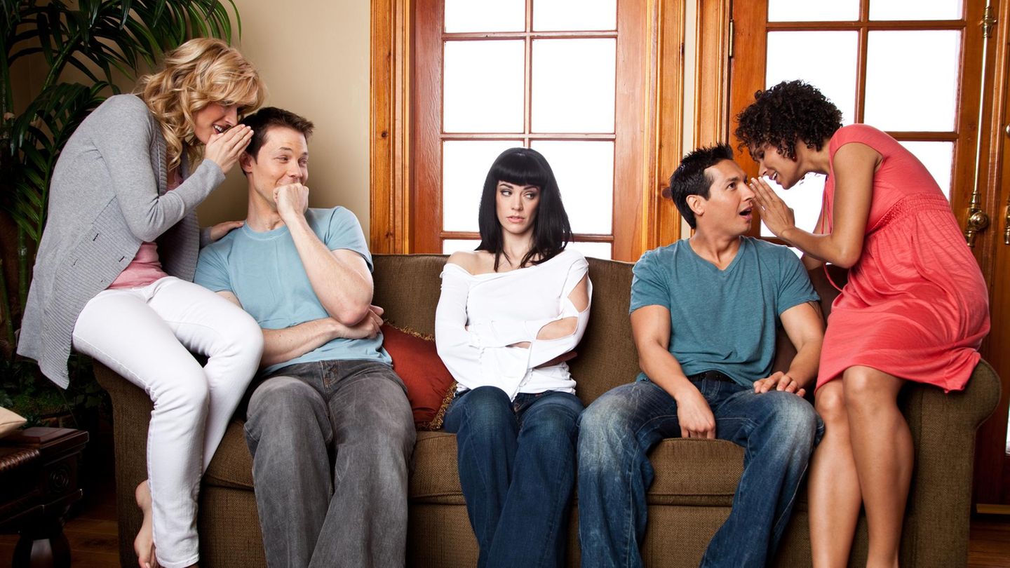 Fünf Menschen auf einem Sofa, die Paare links und rechts tuscheln, die Frau in der Mitte schaut genervt