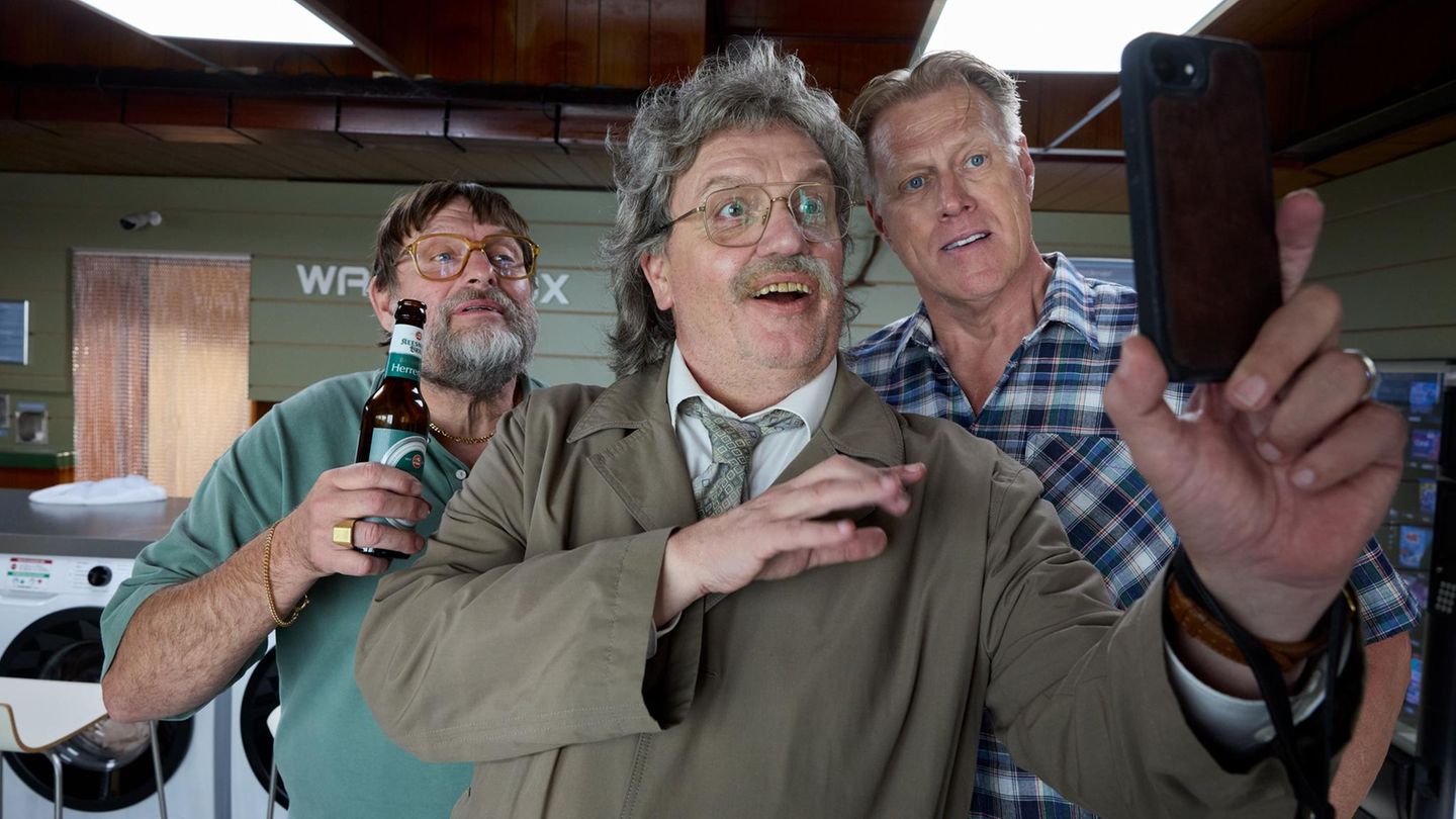 Horst Schlämmer steht mit zwei Männern und schaut in ein Handy