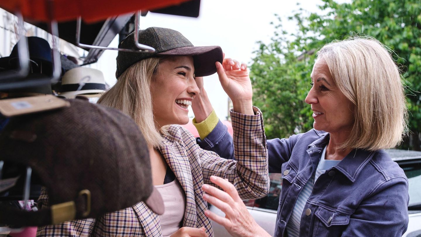 Eine junge Frau probiert eine Mütze auf, während ihre Mutter dabei zuschaut