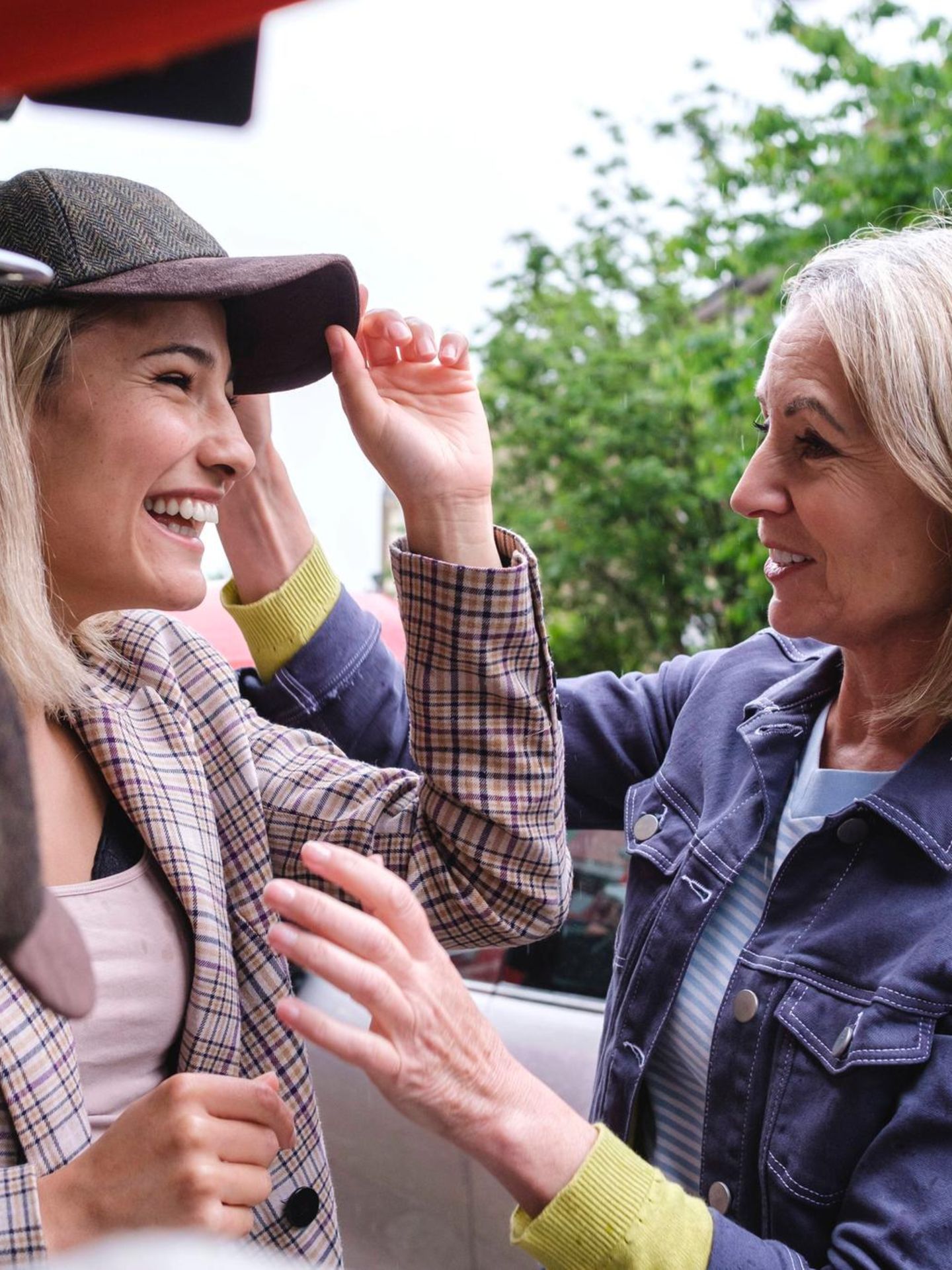 Eine junge Frau probiert eine Mütze auf, während ihre Mutter dabei zuschaut