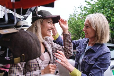 Eine junge Frau probiert eine Mütze auf, während ihre Mutter dabei zuschaut