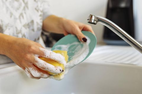 Eine Hand spült mit schaumigem Geschirrspülmittel