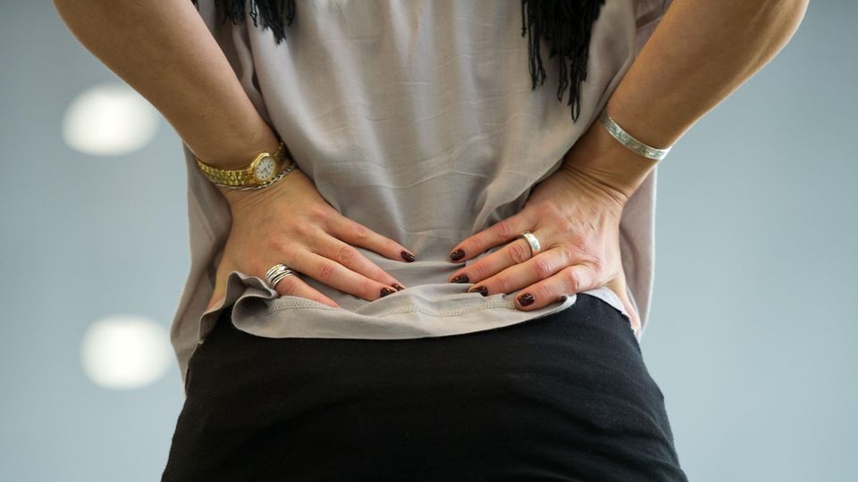 Eine Frau hält sich die Hände an den unteren Rücken.