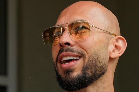 Andrew Tate – ein weißer Mann mit Glatze und Vollbart – lächelt