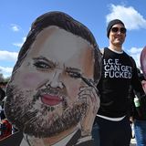 Ein Demonstrierender zeigt Bilder von US-Vizepräsident J. D. Vance und Trump-Berater Stephen Miller mit Hitler-Bart. Was er von der Migrationspolizei ICE hält, steht auf seinem Shirt.
