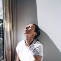 Stress reduzieren, das Gehirn entlasten: Eine Frau lehnt ihren Kopf an der Wand an