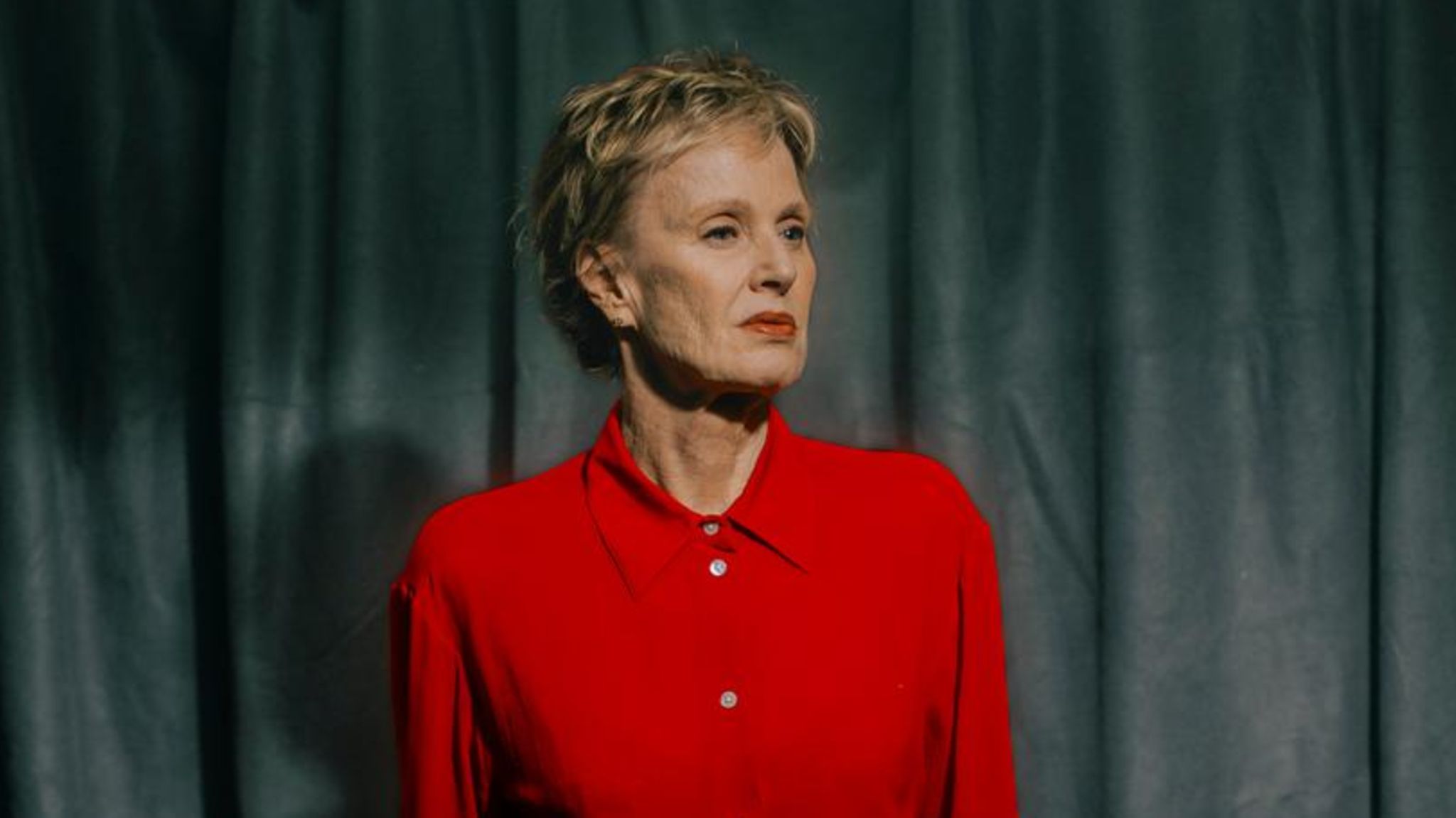 Siri Hustvedt steht für ein Porträtbild vor einem Vorhang schaut zur Seite