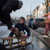 Kinder auf einem Schlitten, bekommen Schlittschuhe angezogen