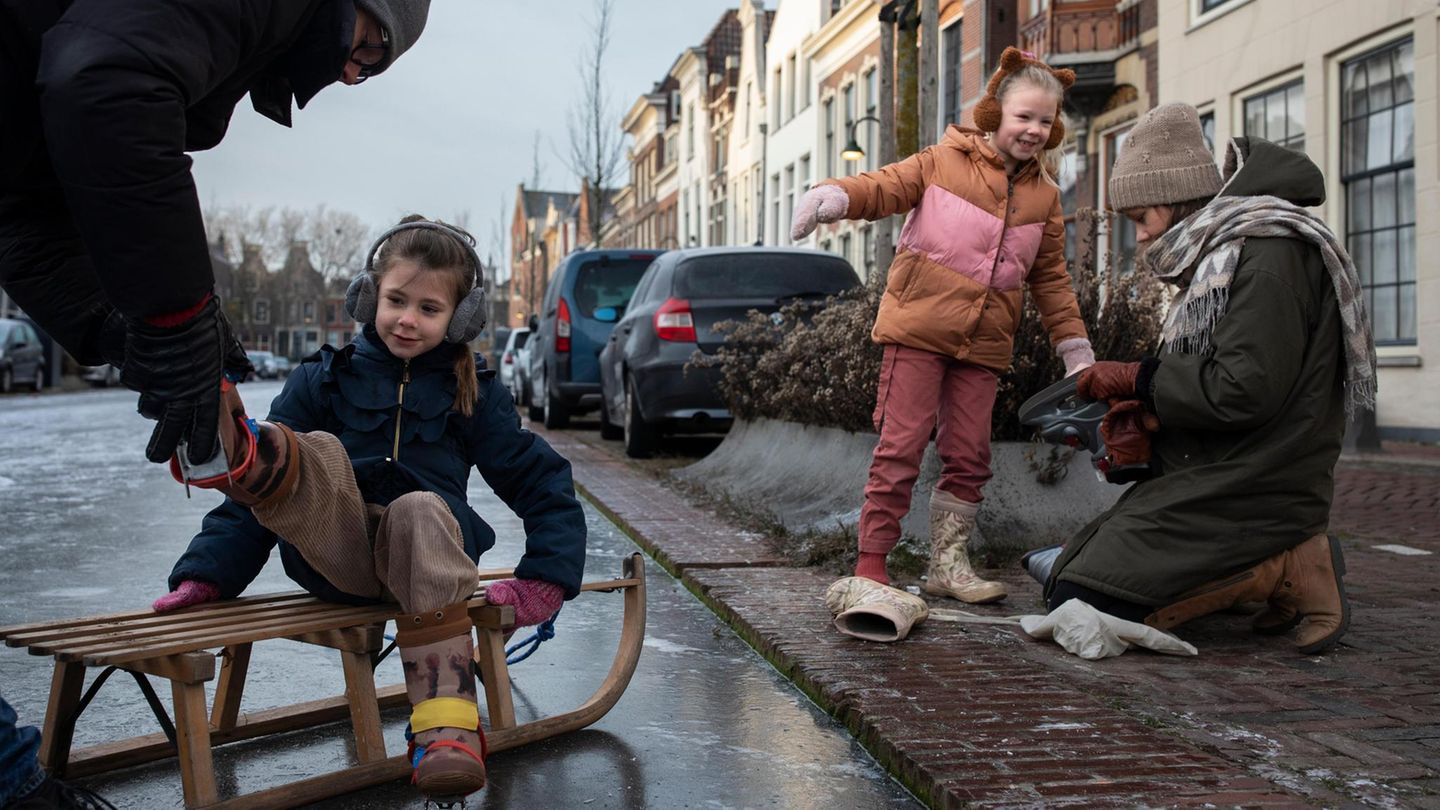 Kinder auf einem Schlitten, bekommen Schlittschuhe angezogen