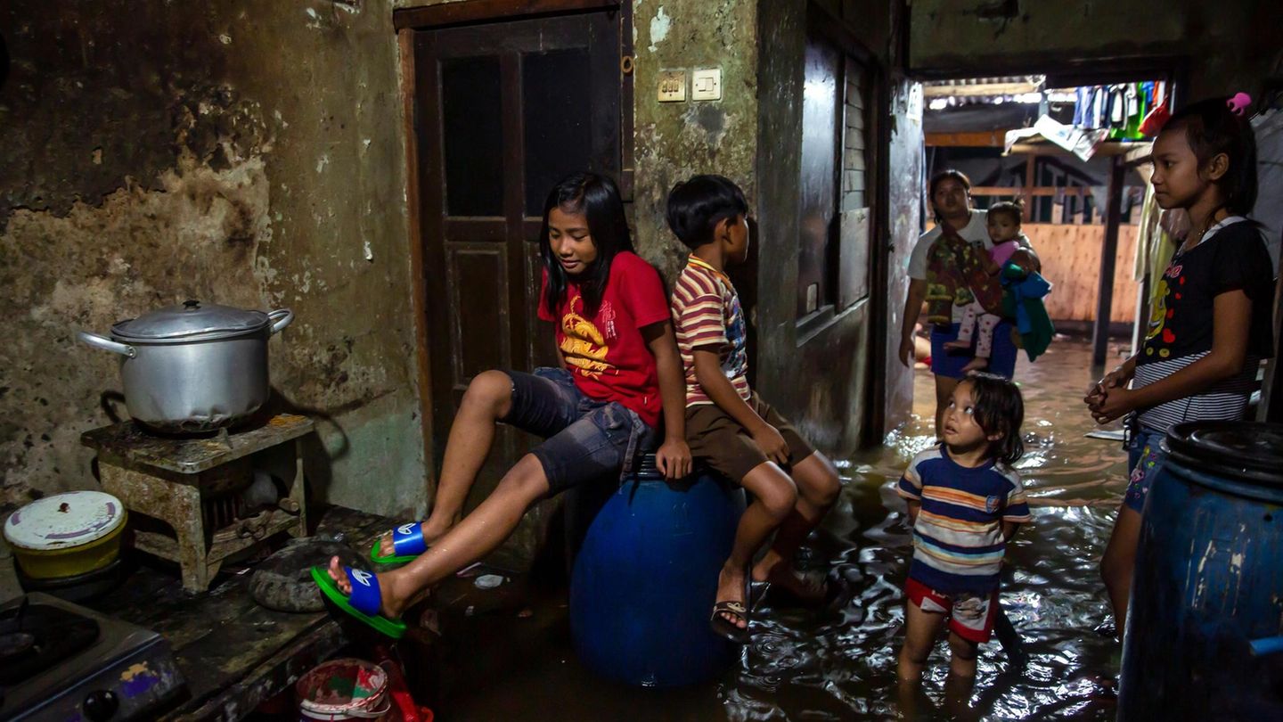 Kinder sitzen auf Regentonnen, Frauen stehen im Wasser