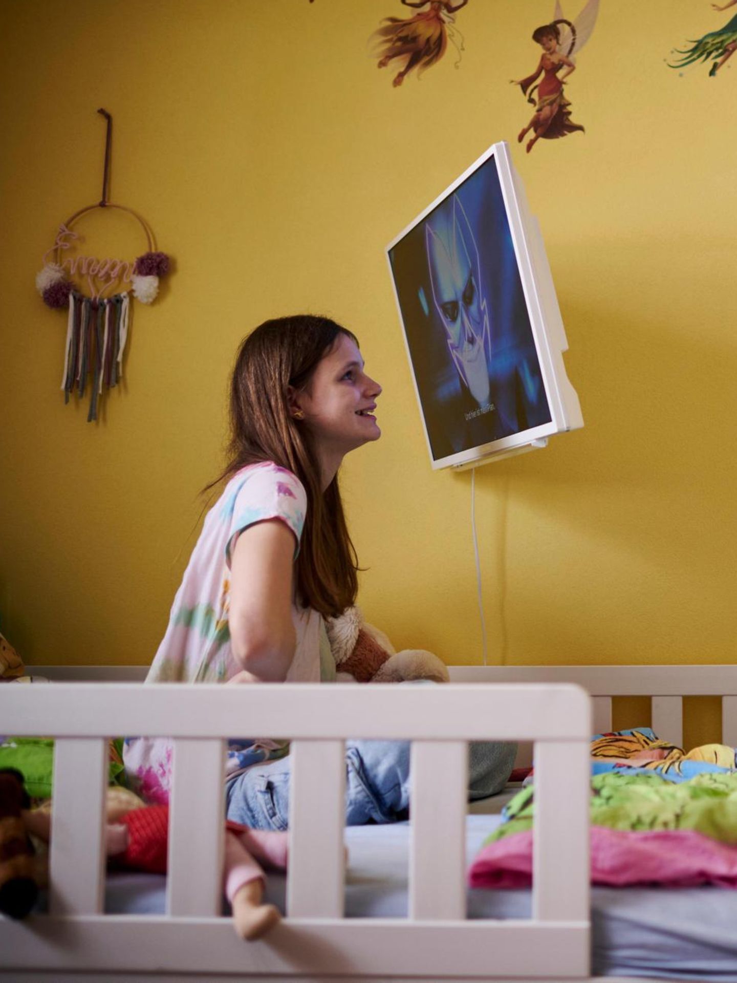 Das Mädchen Emmi sitzt auf eine Bett, nah vor einem Bildschirm. Sie leidet unter Kinderdemenz