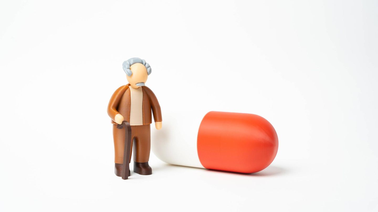 Krankenkassenreform, Symbolzeichnung: Ein alter Herr steht neben einer roten Pille