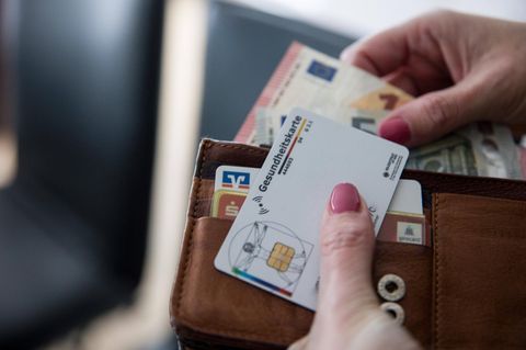 Krankenkassenreform: Eine Hand hält einen Geldbeutel mit Geld und einer Versichertenkarte