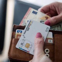 Krankenkassenreform: Eine Hand hält einen Geldbeutel mit Geld und einer Versichertenkarte