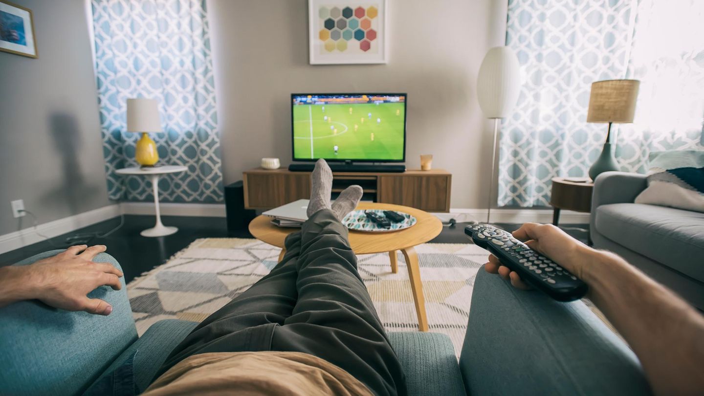 Ein Mann sitzt im Wohnzimm er und schaut auf dem Fernseher Fußball