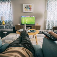 Ein Mann sitzt im Wohnzimm er und schaut auf dem Fernseher Fußball