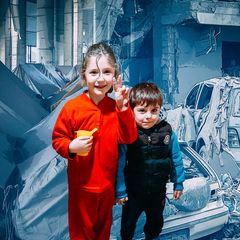 Montage: Zwei Kinder vor einem geteilten Hintergrund: Links Zelte als Notunterkunft, rechts zerstörte Autos im Libanon