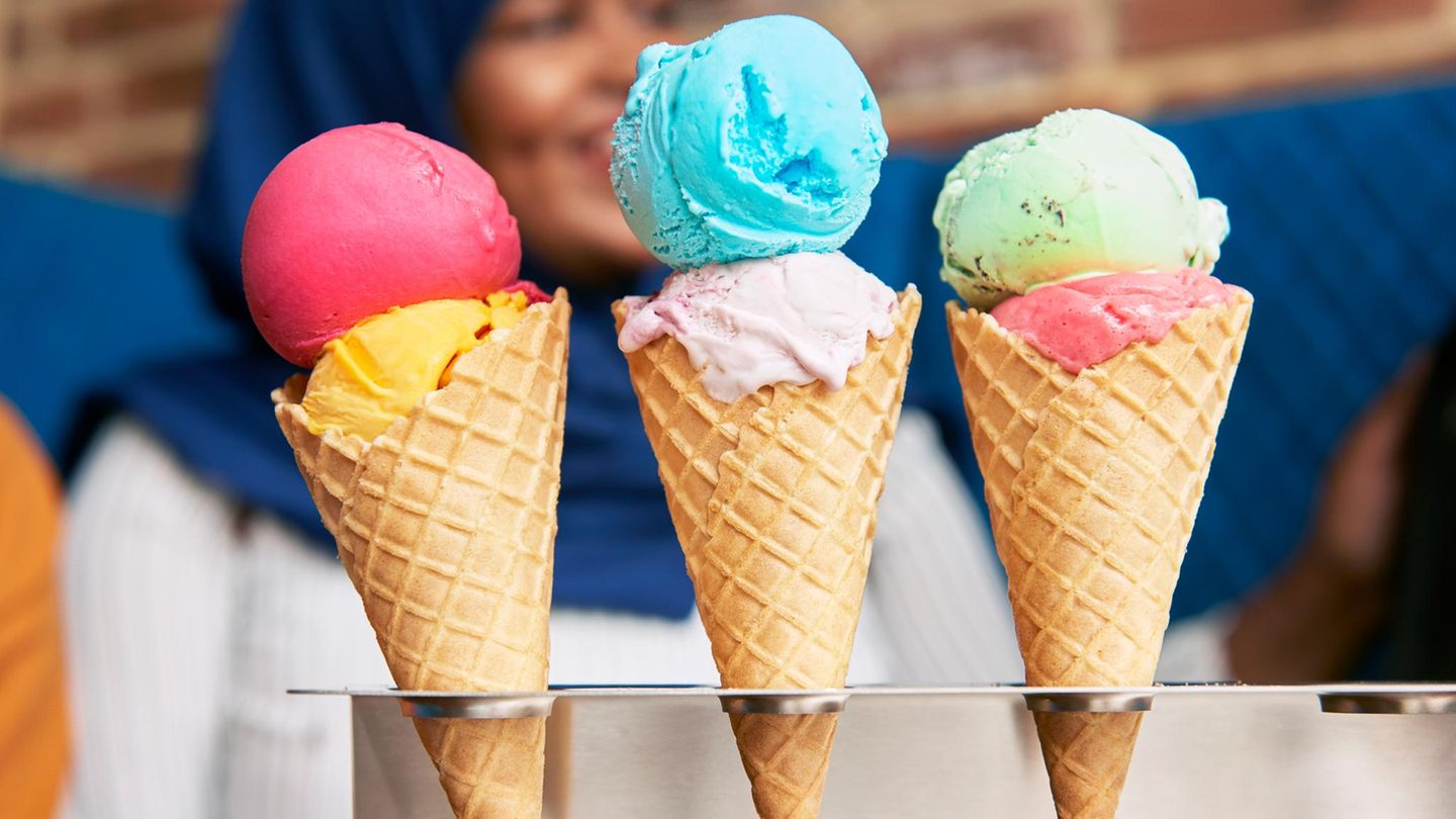 In einer Eisdiele stehen drei Hörnchen mit buntem Eis in einem Ständer