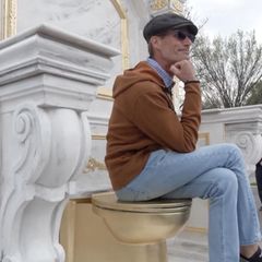 Ein Mann sitzt auf einer goldenen Kloschüssel