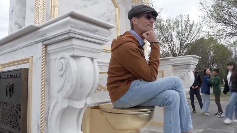 Ein Mann sitzt auf einer goldenen Kloschüssel