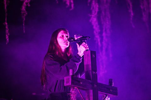 Ethel Cain performt auf einer Bühne, während sie an einem Holzkreuz lehnt