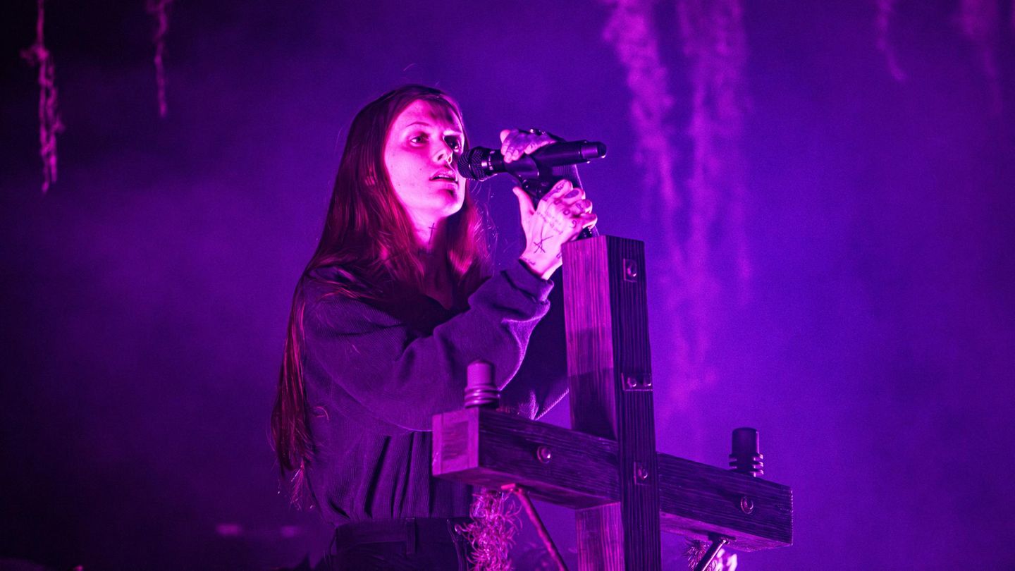 Ethel Cain performt auf einer Bühne, während sie an einem Holzkreuz lehnt