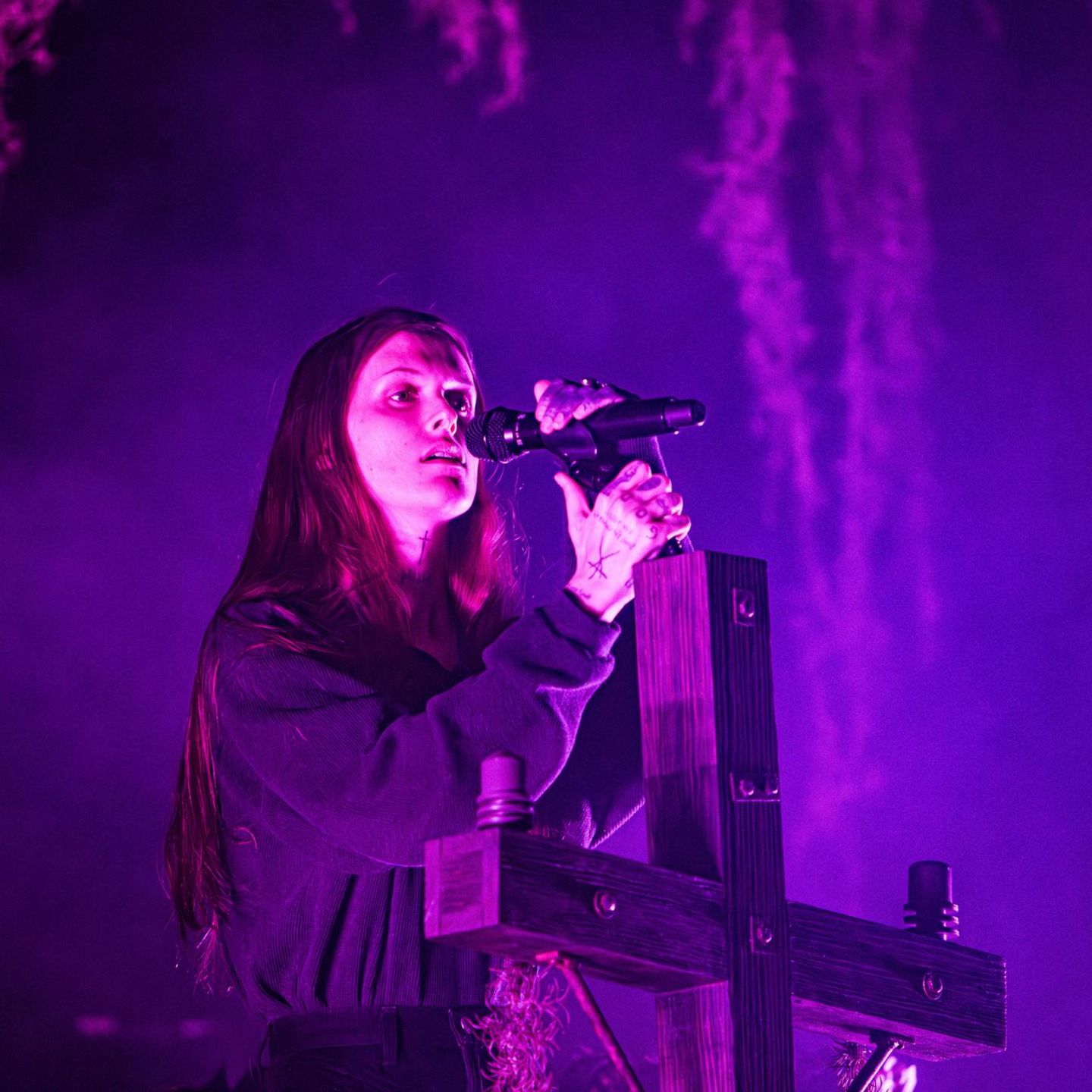 Ethel Cain performt auf einer Bühne, während sie an einem Holzkreuz lehnt