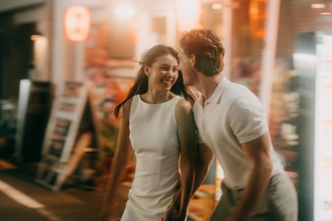 Ein Paar läuft lachend über die Straße. Dahinter sind keine Frauen und Männer zu sehen