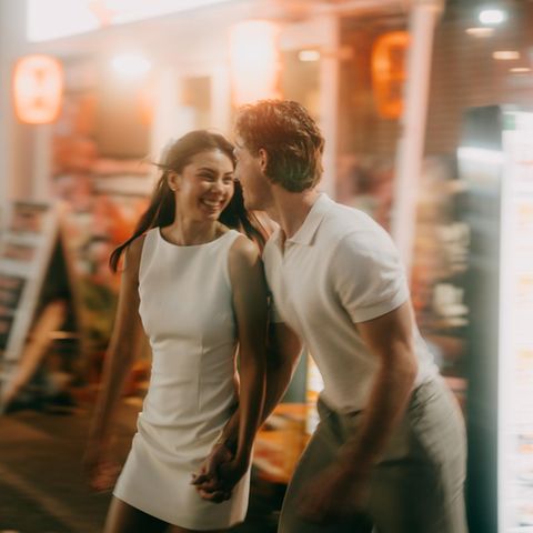 Ein Paar läuft lachend über die Straße. Dahinter sind keine Frauen und Männer zu sehen