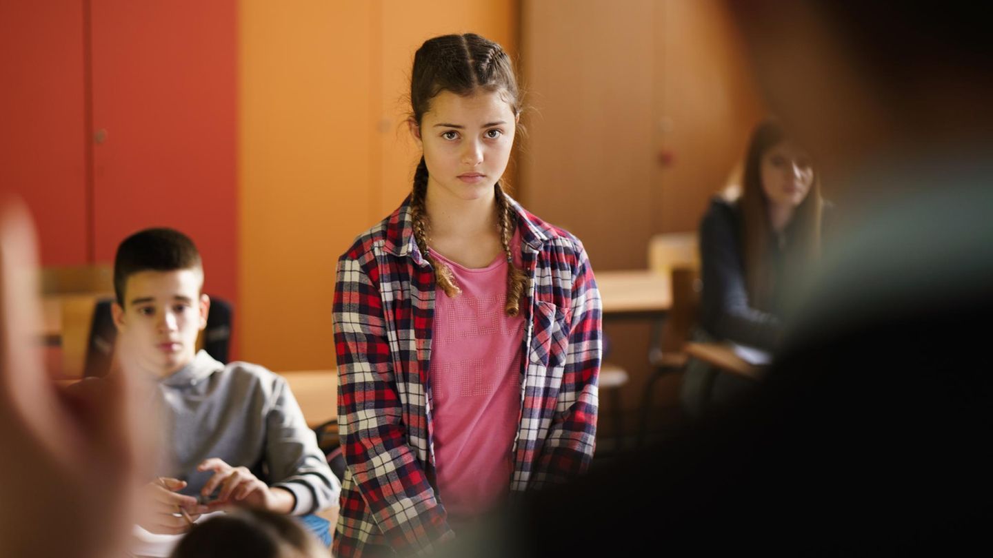 Mädchen steht in der Klasse, Gesichtsausdruck besorgt. Narzissmus kommt auch bei Lehrkräften vor.