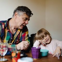 Erziehung: Großvater sitzt mit Enkeltochter am Tisch