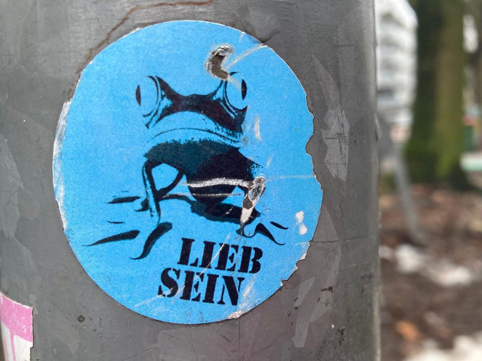 Blauer Aufkleber eines Froschs mit der Zeile "Lieb sein"