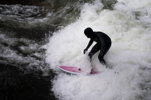 Ein Surfer in schwarzem Neopren surft auf pink-weißem Board die Eisbachwelle in München
