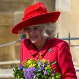 Königin Camilla trägt ein rotes Kostüm und hält einen Blumenstrauß in den Händen