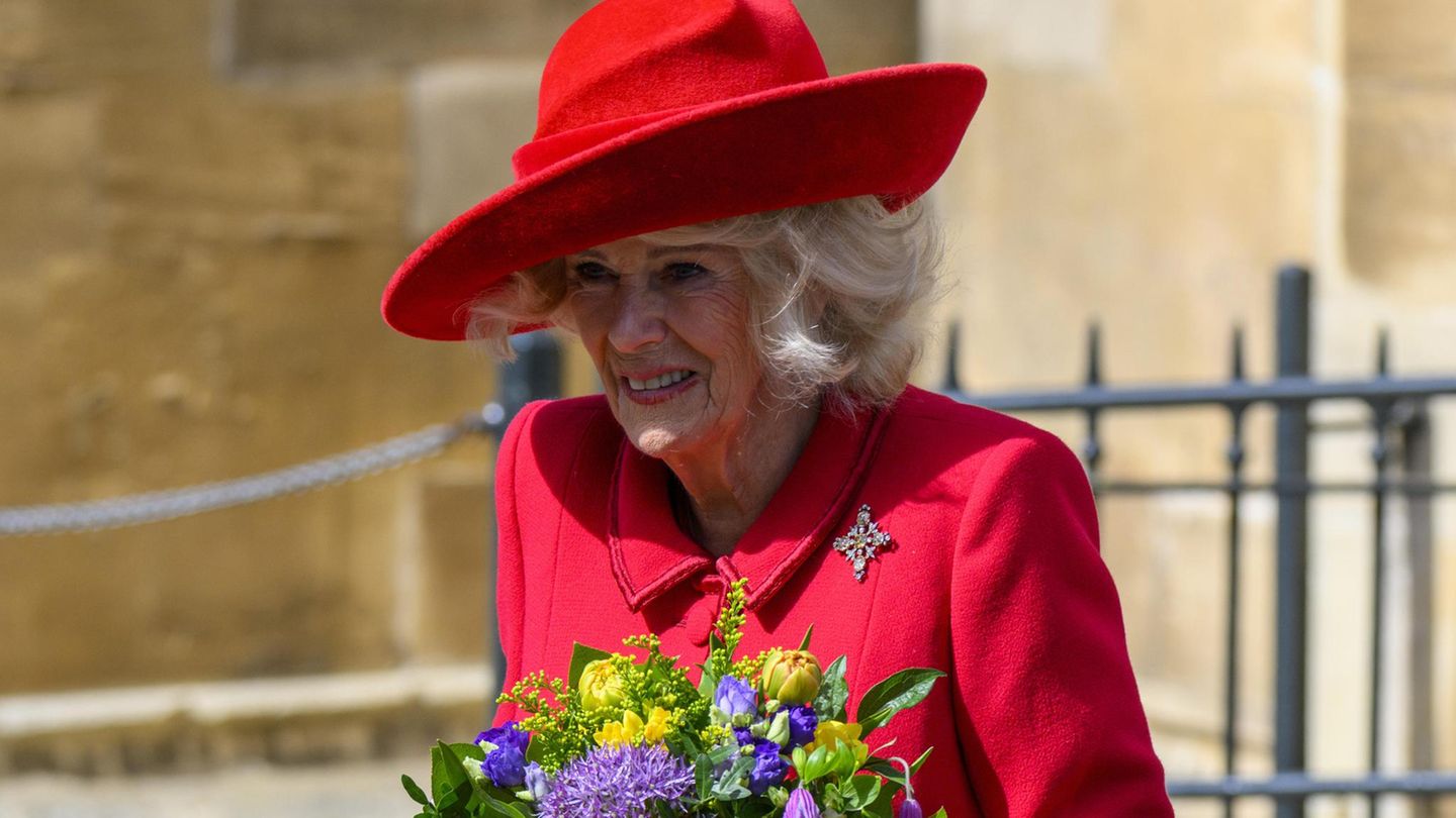 Königin Camilla trägt ein rotes Kostüm und hält einen Blumenstrauß in den Händen