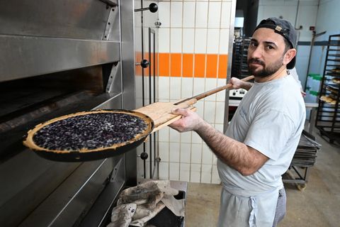 Bäcker Sulaiman Shapal nimmt ein Blech mit Blaubeerkuchen aus einem Ofen in einer Backstube. Er ist aus Syrien nach Deutschland