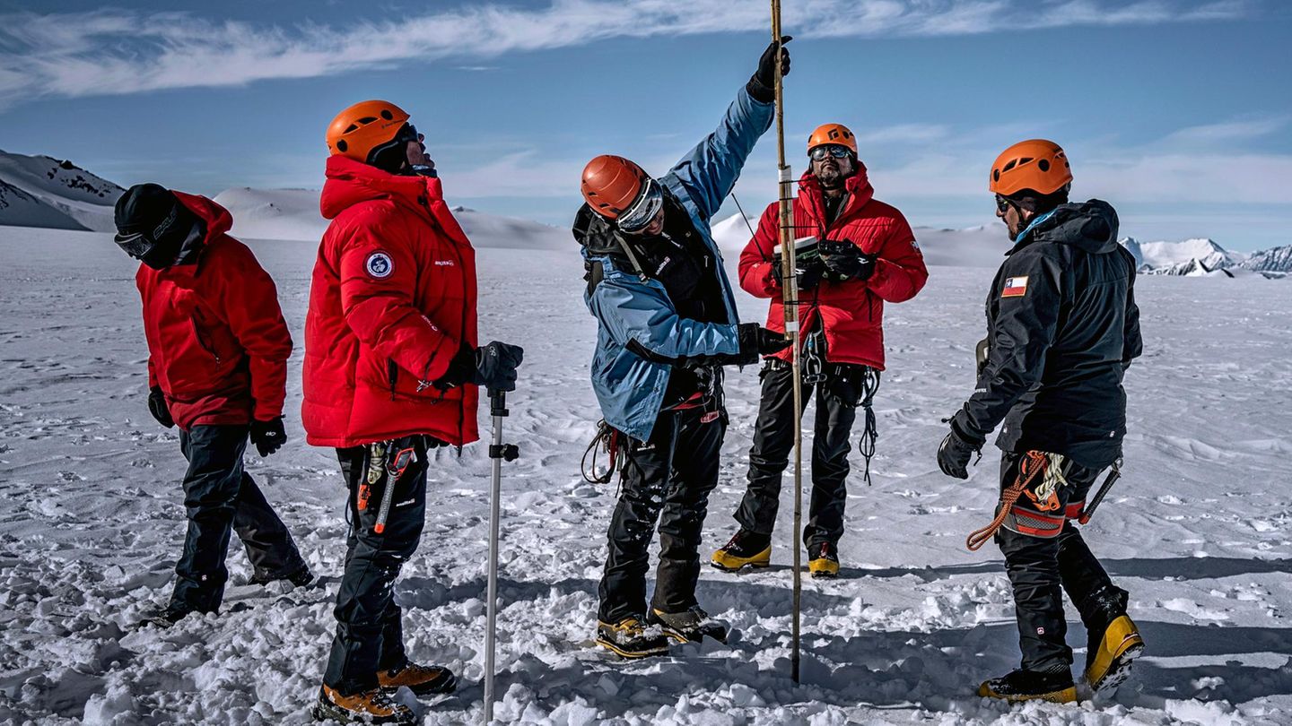 In der Antarktis markiert Forscher Jaña Messpunkte mit Bambusstäben, drumherum stehen mehrere Menschen