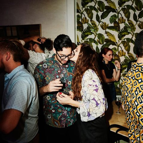 Partyszene: Eine Frau küsst einen Mann, andere Gäste stehen im Hintergrund. Ist es Liebe?