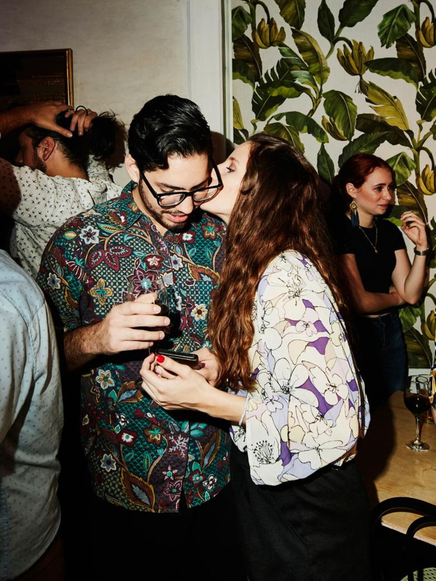 Partyszene: Eine Frau küsst einen Mann, andere Gäste stehen im Hintergrund. Ist es Liebe?