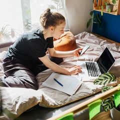 Eine Jugendliche sitzt in ihrem Bett mit Laptop und Smartphone: Social Media liefert Ablenkung