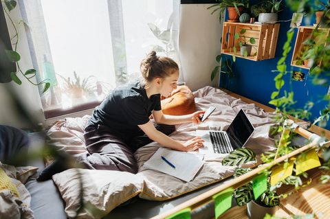 Eine Jugendliche sitzt in ihrem Bett mit Laptop und Smartphone: Social Media liefert Ablenkung