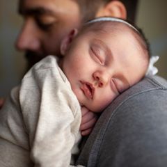 ein kleines Baby liegt auf der Schulter eines Mannes