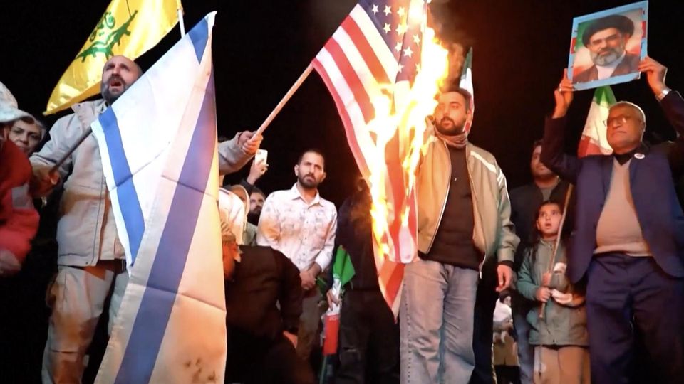 Iranische Regime-Anhänger feiern auf den Straßen und zünden eine USA-Flagge an.