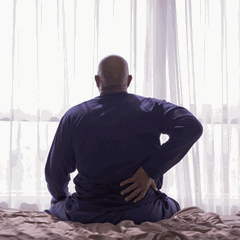 Ein Mann sitzt auf einem Bett und hält sich den Rücken