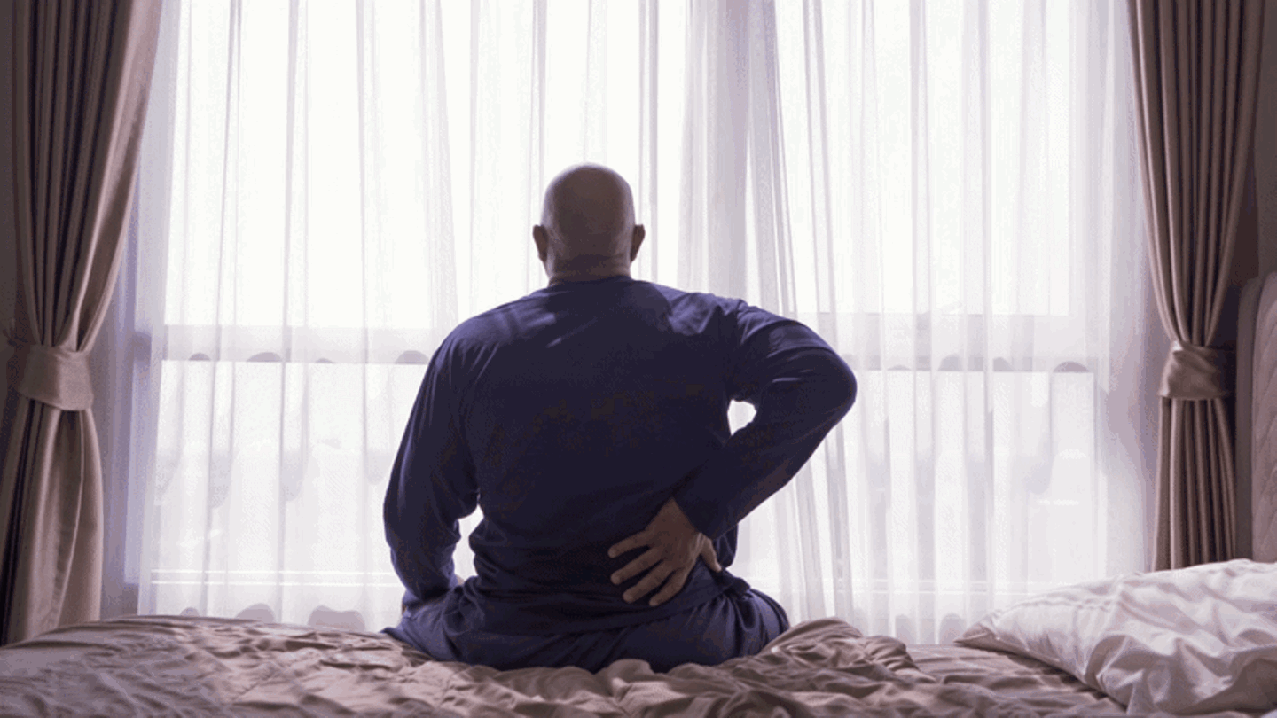 Ein Mann sitzt auf einem Bett und hält sich den Rücken