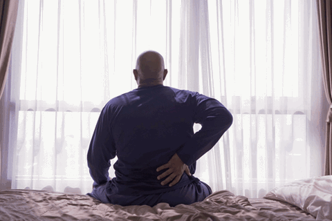 Ein Mann sitzt auf einem Bett und hält sich den Rücken