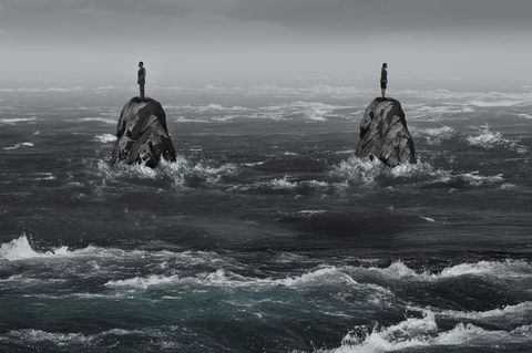 Zwei Felsen im Ozean, darauf steht je eine Person